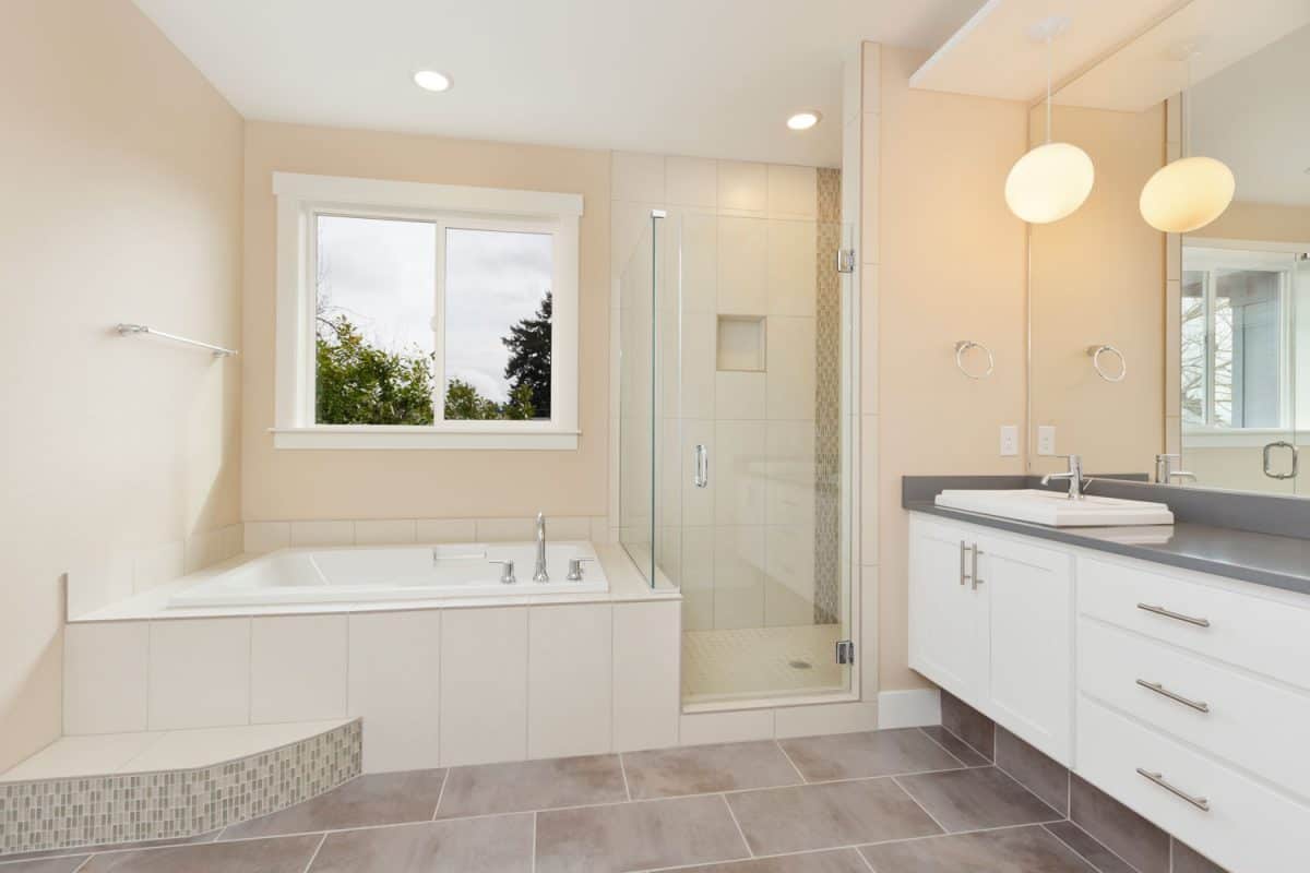 Interior of a beige colored bathroom with a glass walled shower area and a fitter bathtub