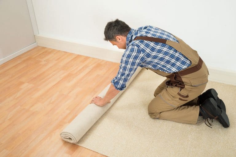 Male Worker Unrolling Carpet On Floor At Home, Can You Install Carpet Without Removing Baseboards?