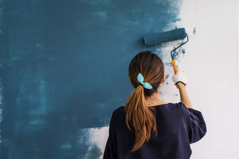 Young asian happy woman painting interior wall with paint roller in new house, Can You Use Acrylic Paint On Walls [Indoor And Outdoor Applications]
