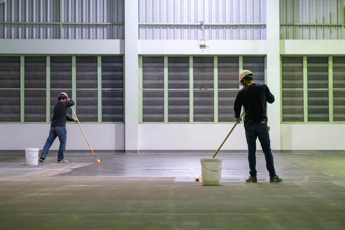 Construction worker using roller spreading epoxy primer for self-leveling method of epoxy floor