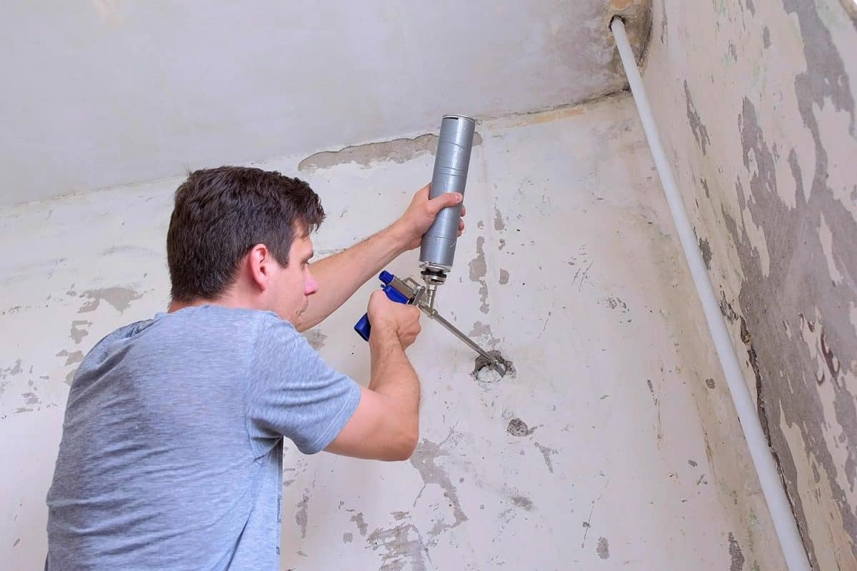 Man fills hole in wall of concrete slab mounting foam making repairs at home