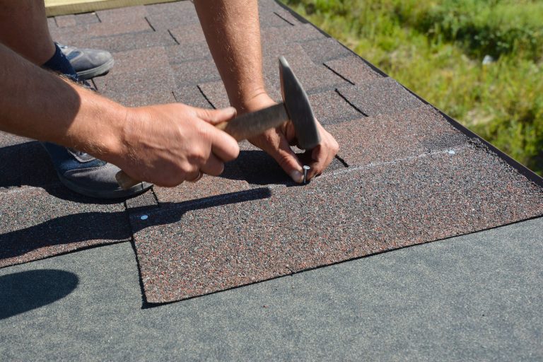 Roofer installing Asphalt Shingles on a house construction roof corner with a hammer and nails, How To Seal Roofing Nails
