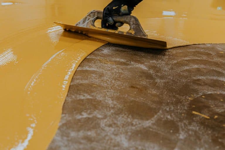 A worker coating floor with self-leveling epoxy resin in industrial workshop, Epoxy Flooring Pros And Cons [A Comprehensive Review of This Versatile Floor Coating]