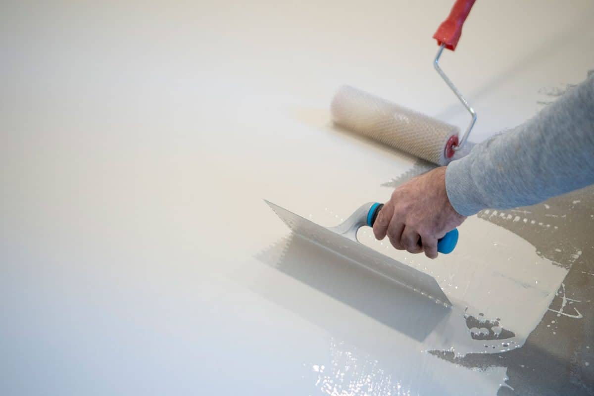 Worker using a trowel and roller to spread the white epoxy on the floor