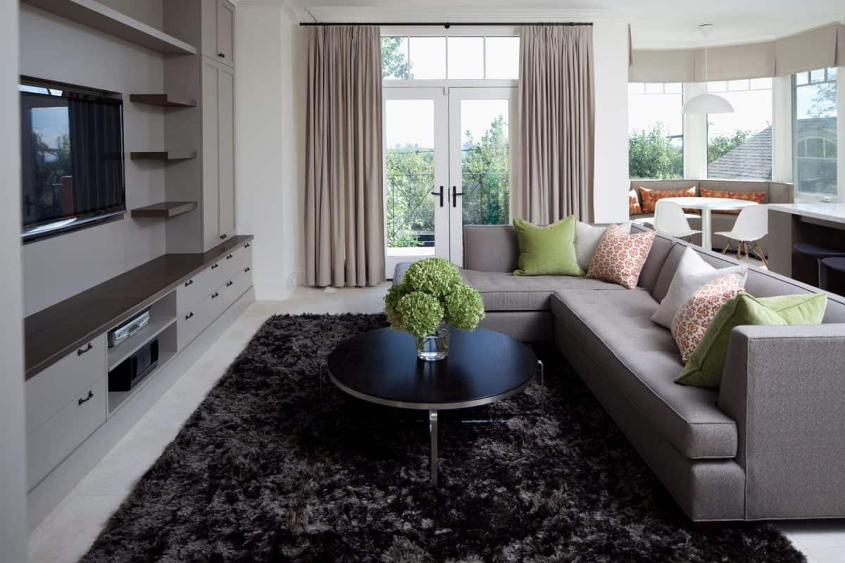 A bright and luxurious living area with a black rug, gray sectional sofa and a matching round metal coffee table