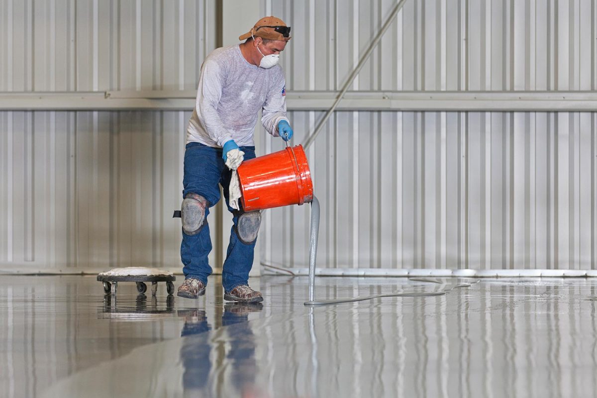 A construction worker pours paint onto a warehouse floor