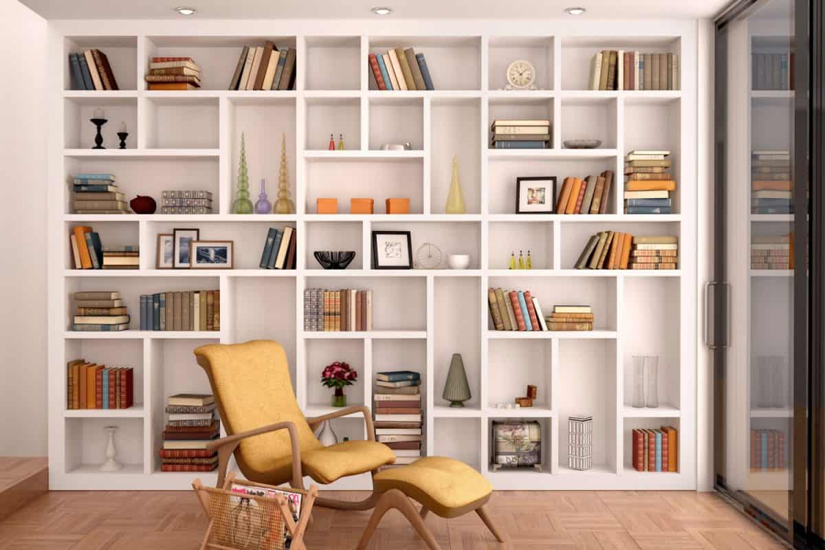 A huge bookcase inside a study room and a small reading chair with a book holder on the side