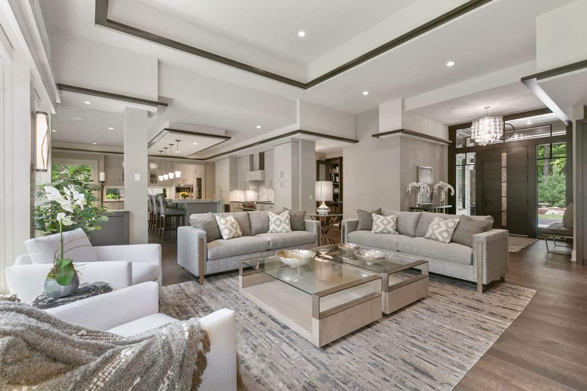 A luxurious open space living area with wooden flooring, carpeted area with gray couches and patterned throw pillows