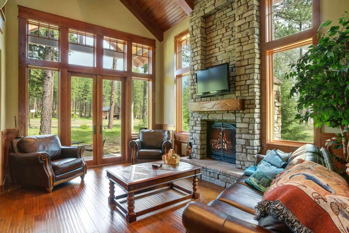 A rustic living area with hardwood flooring, tan walls with wooden door and window frames and a stone decorated fireplace