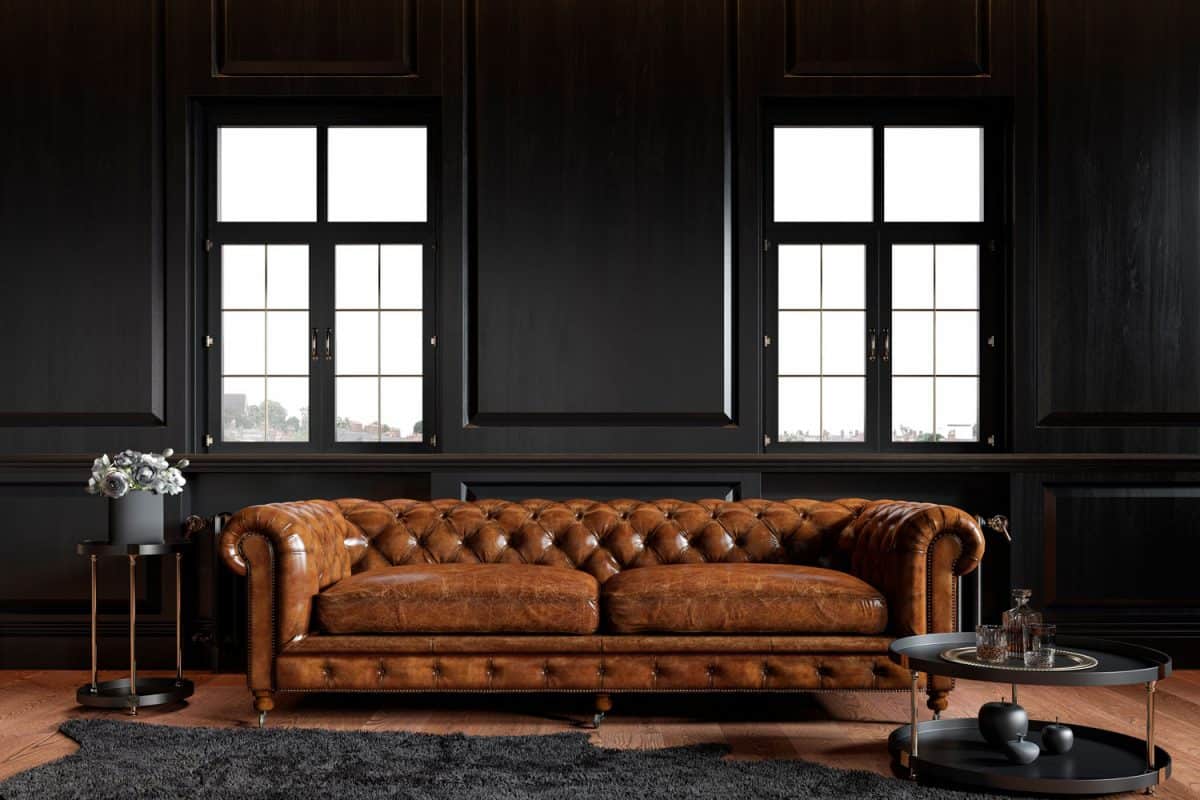 A shiny brown leather sofa inside a rustic living room with black flat panel walls 