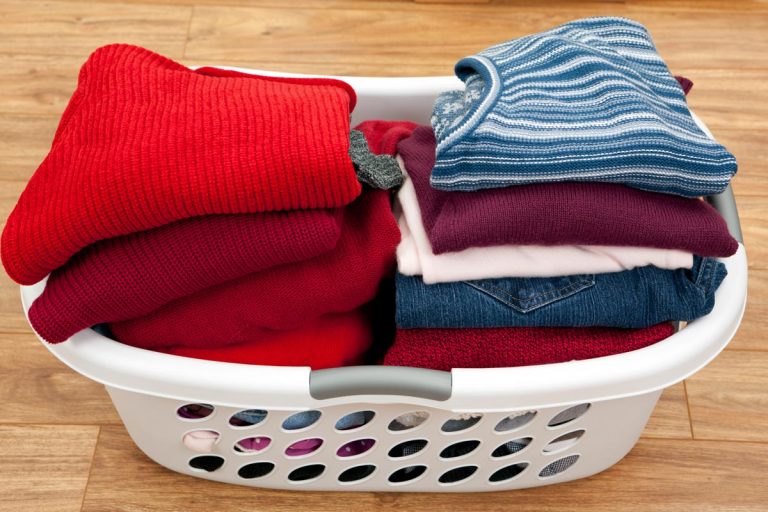 A folded blue jeans, sweaters, and vests in the laundry basket, 4 Best Places To Keep Your Laundry Basket