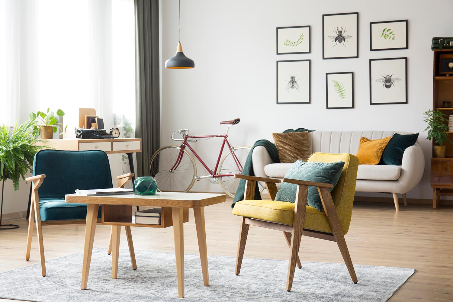Retro armchairs at wooden table on grey carpet in living room with lamp, bike and posters