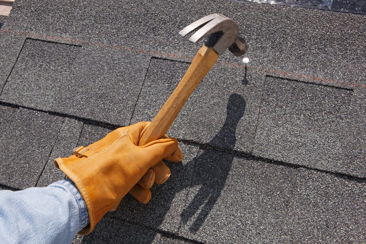 Roof installer using a hammer to install asphalt shingles