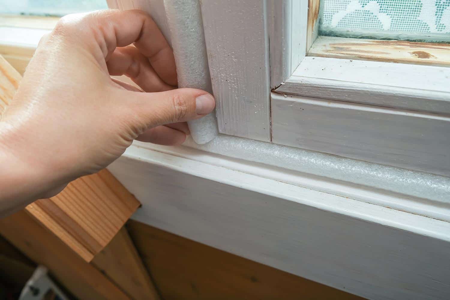 Woman hand insulating old windows to prevent warmth heat leak and drafts