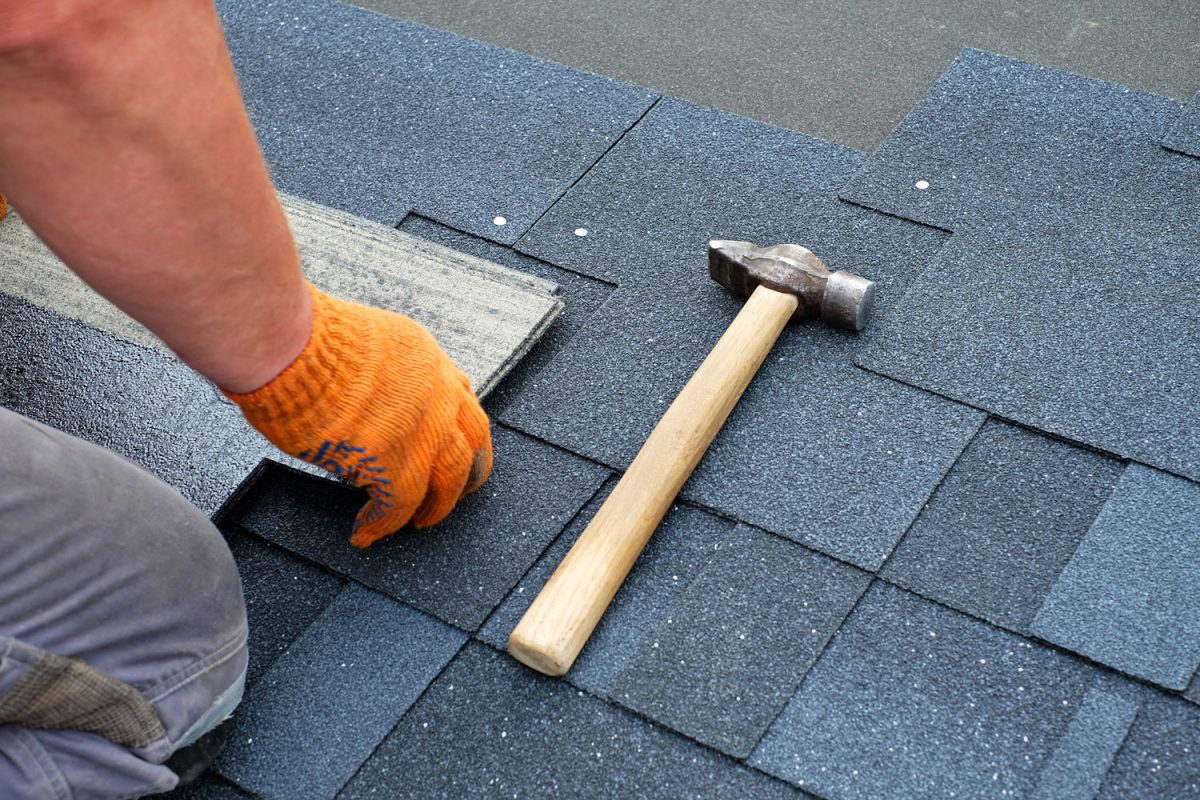 Worker laying out asphalt shingles on the roof