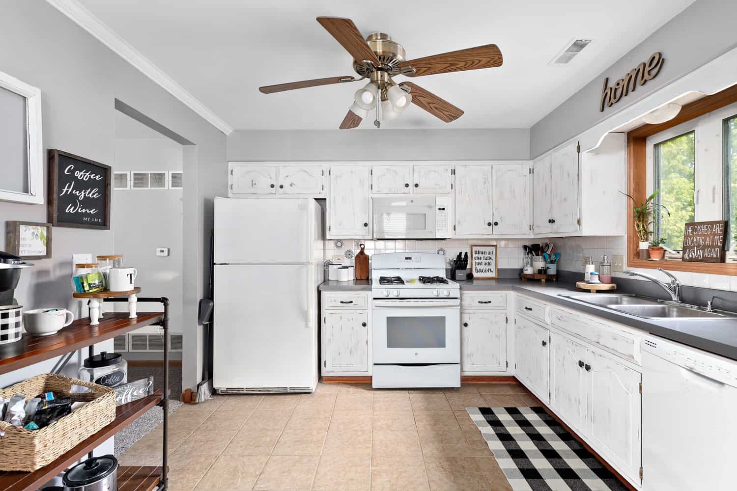 A renovated farmhouse kitchen with white cabinets, white appliances, tile flooring, and decorations throughout.