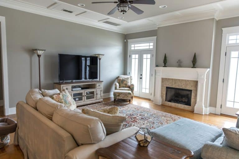 A classic and American country home with hardwood flooring, tan leather sofas with gray painted walls, How High Should A Fireplace Mantel Be?