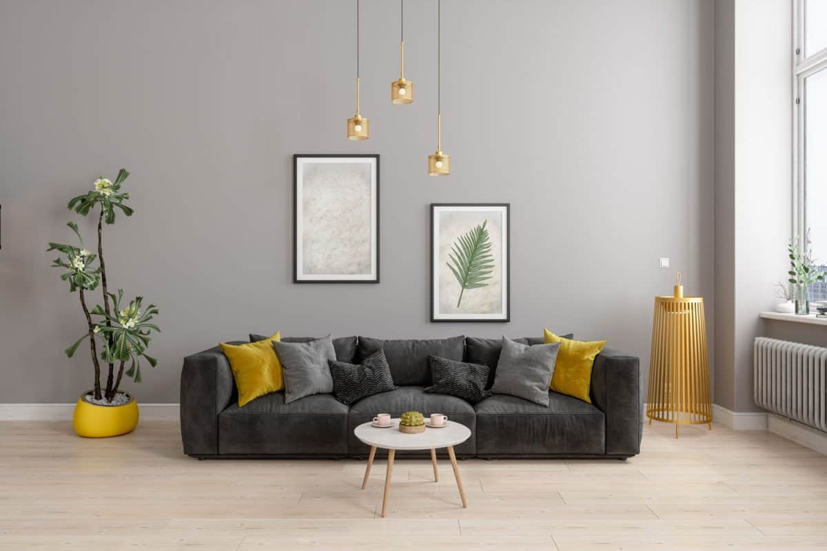 A dark gray sofa with matching gray and yellow pillows with dangling lamps inside a gray living room