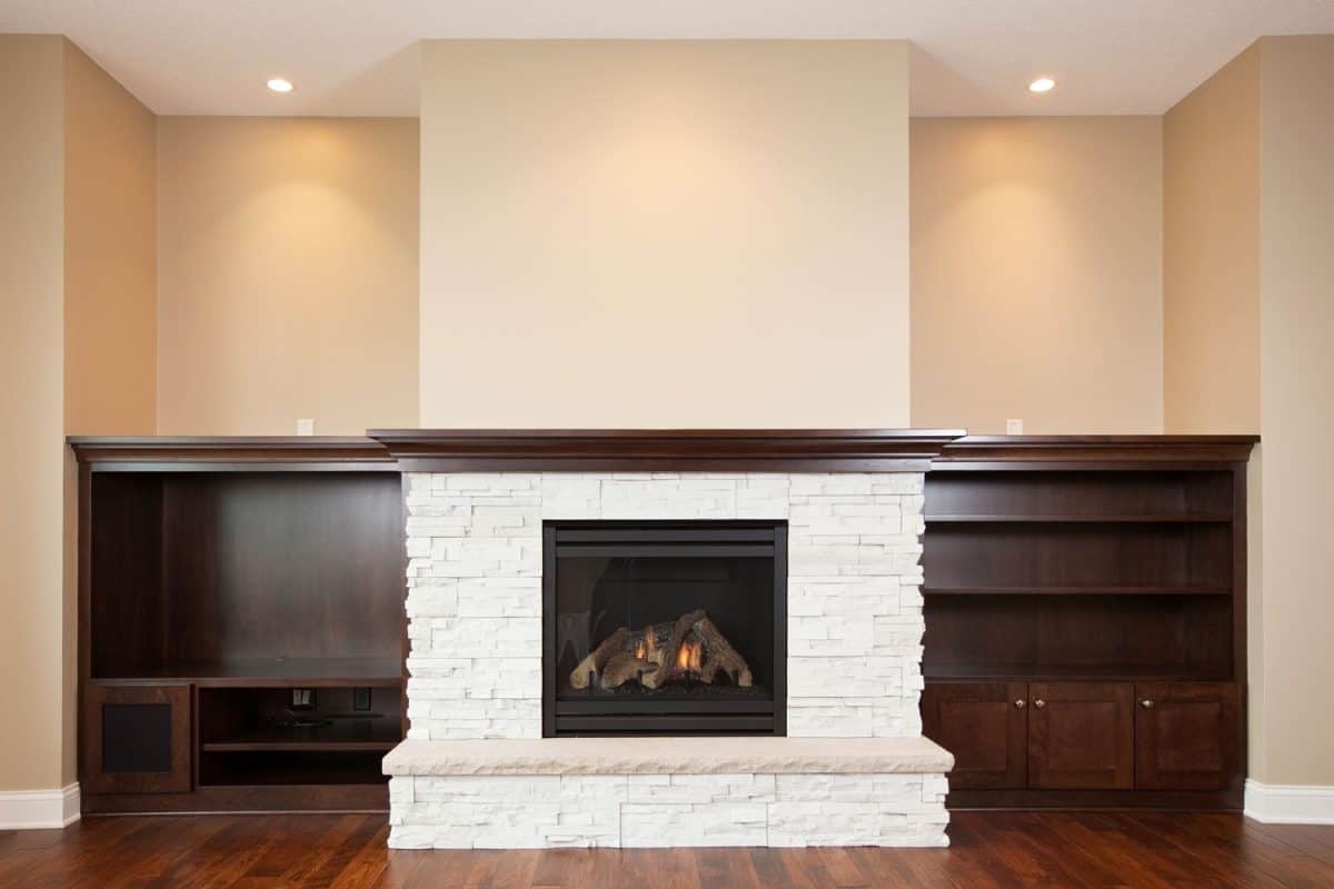 An empty living area with a white fireplace and wood burning inside it