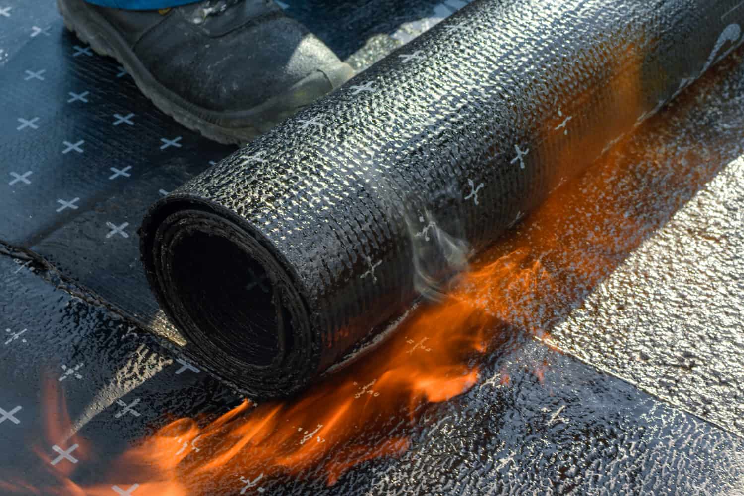 Construction worker heating and melting bitumen rolls.