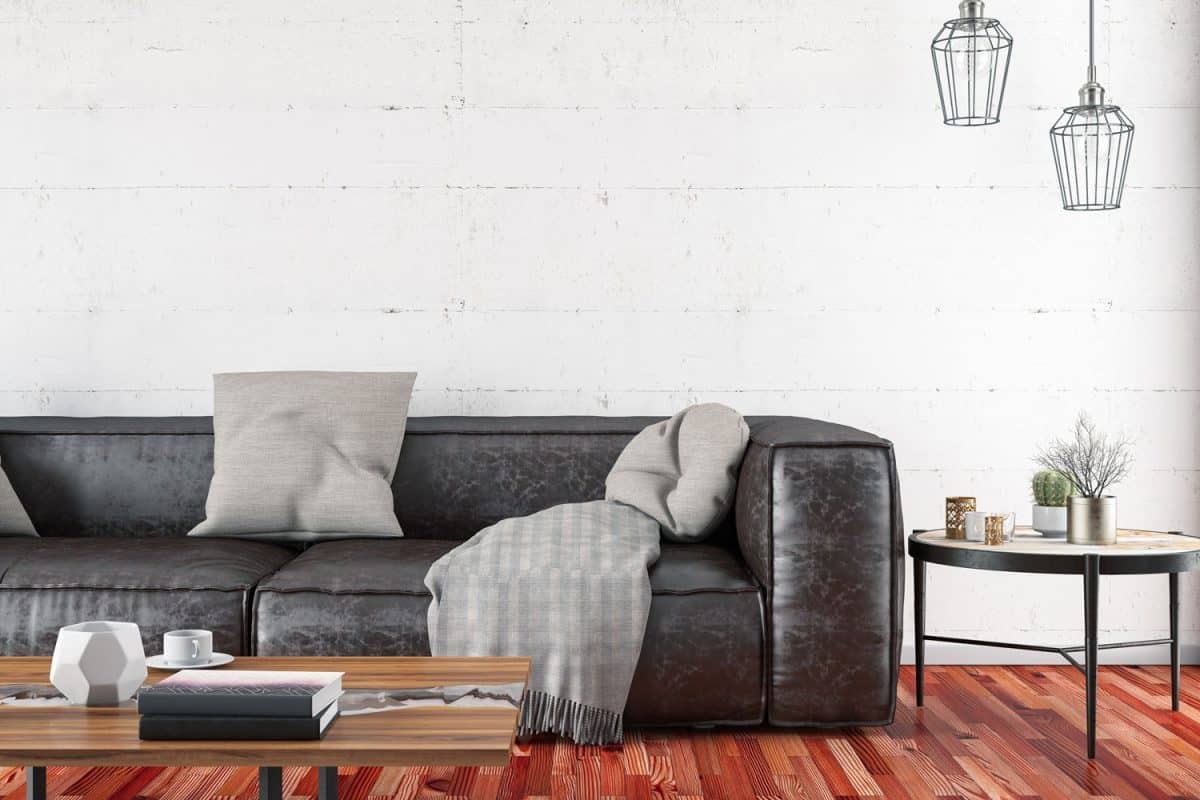 Dark gray leather sofa with gray throw pillows and throw inside a wooden flooring room