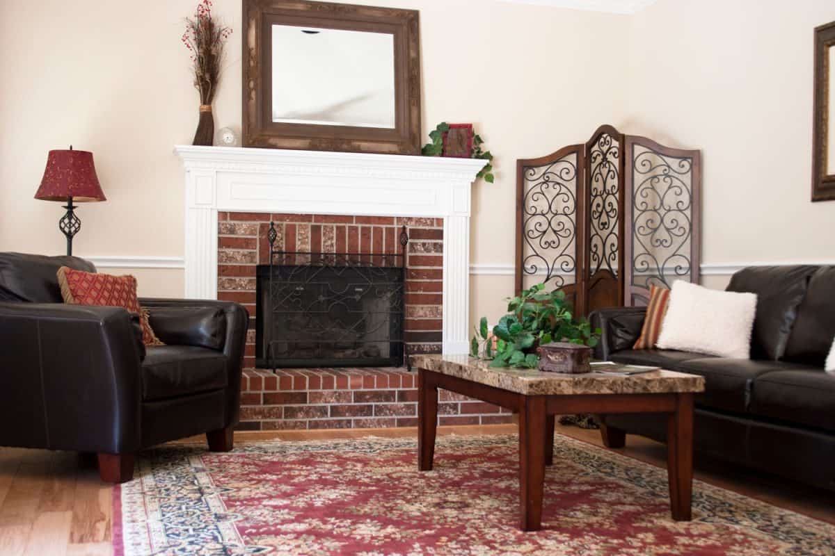 Interior of a living area with a fireplace with a black leather armchair and rug up front of the fireplace