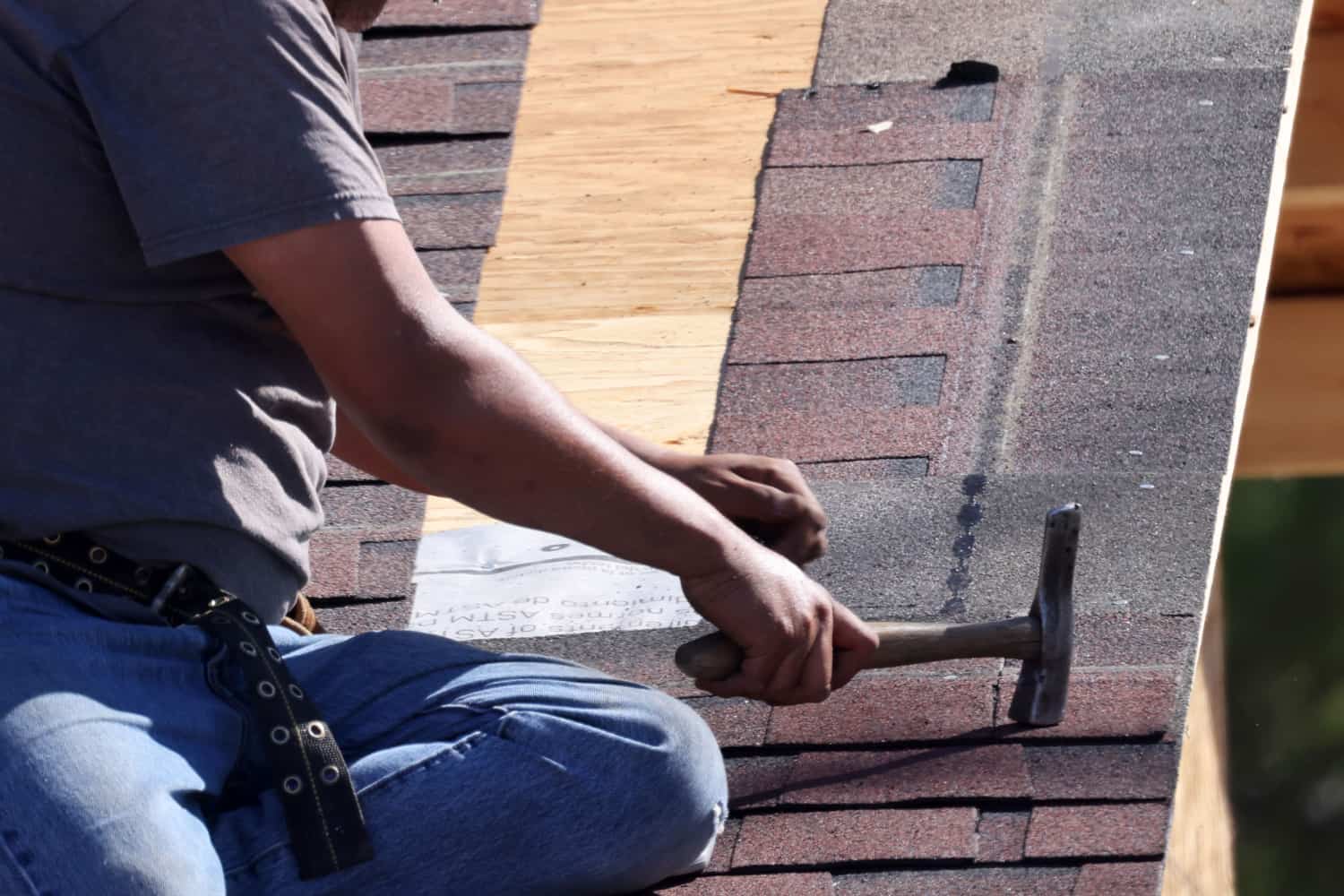 Man nailing shingles on roof with roofing hammer