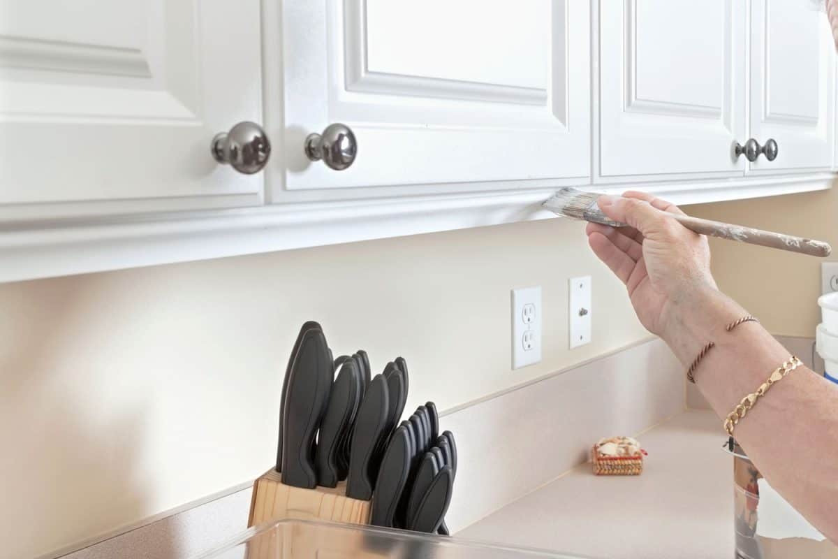 Man painting the oak kitchen cabinets with white and kitchen utensils on the countertop
