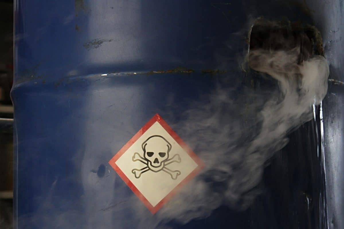 Poisonous toxic gas and water leaking from damaged blue steel barrel, sign of toxic material on barrel surface