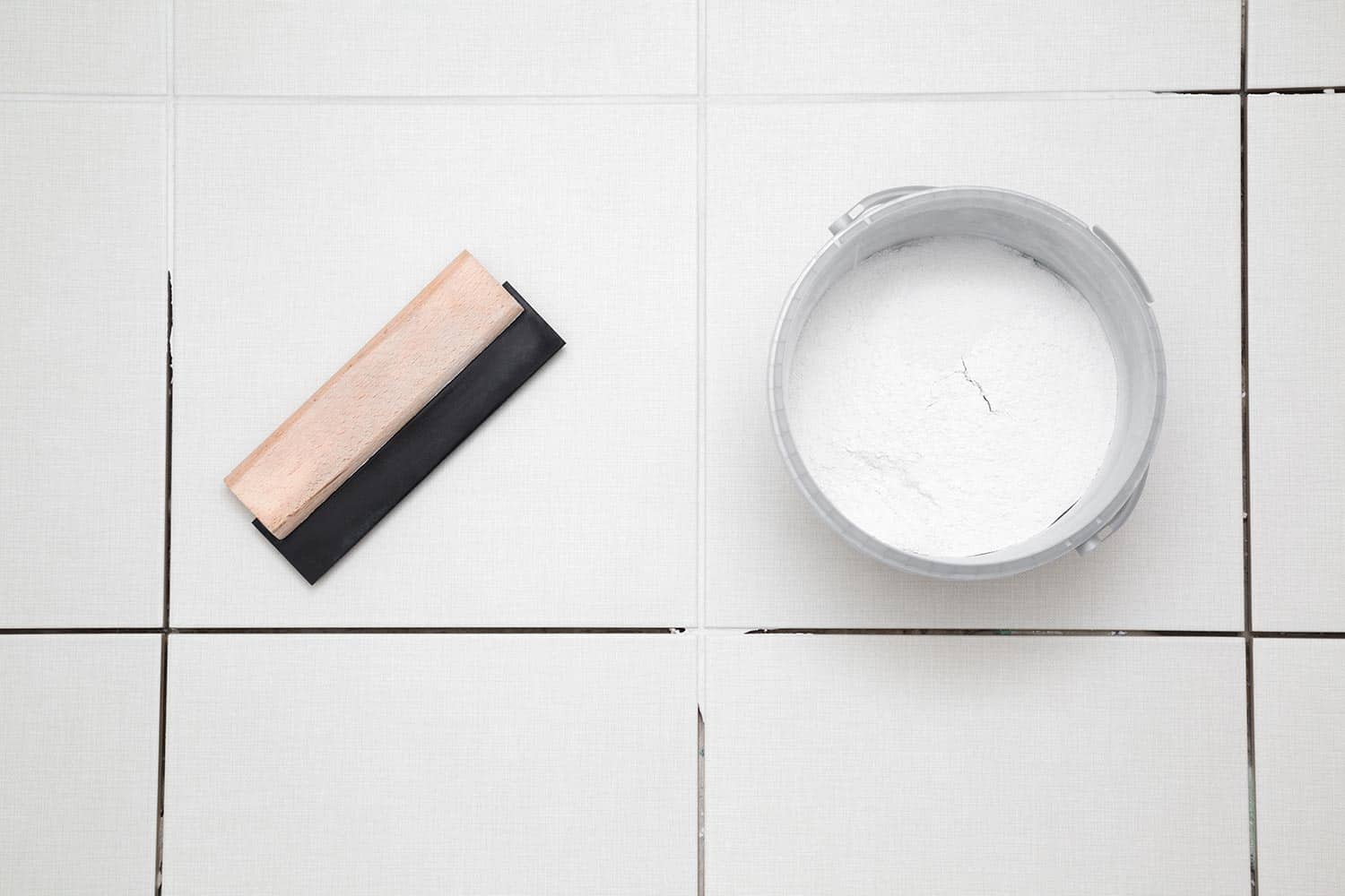 Rubber trowel and container with powder of grouting paste for ceramic tile seams on floor