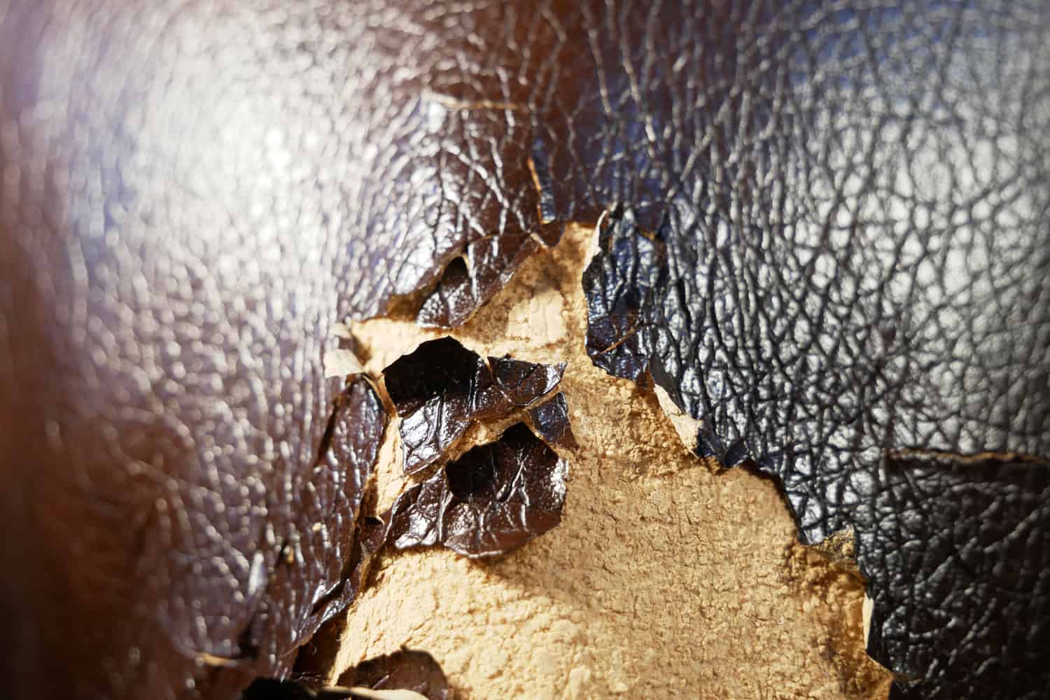 Shabby and worn brown faux leather texture background with cracks and damages, repairman background. Peeling faux leather couch