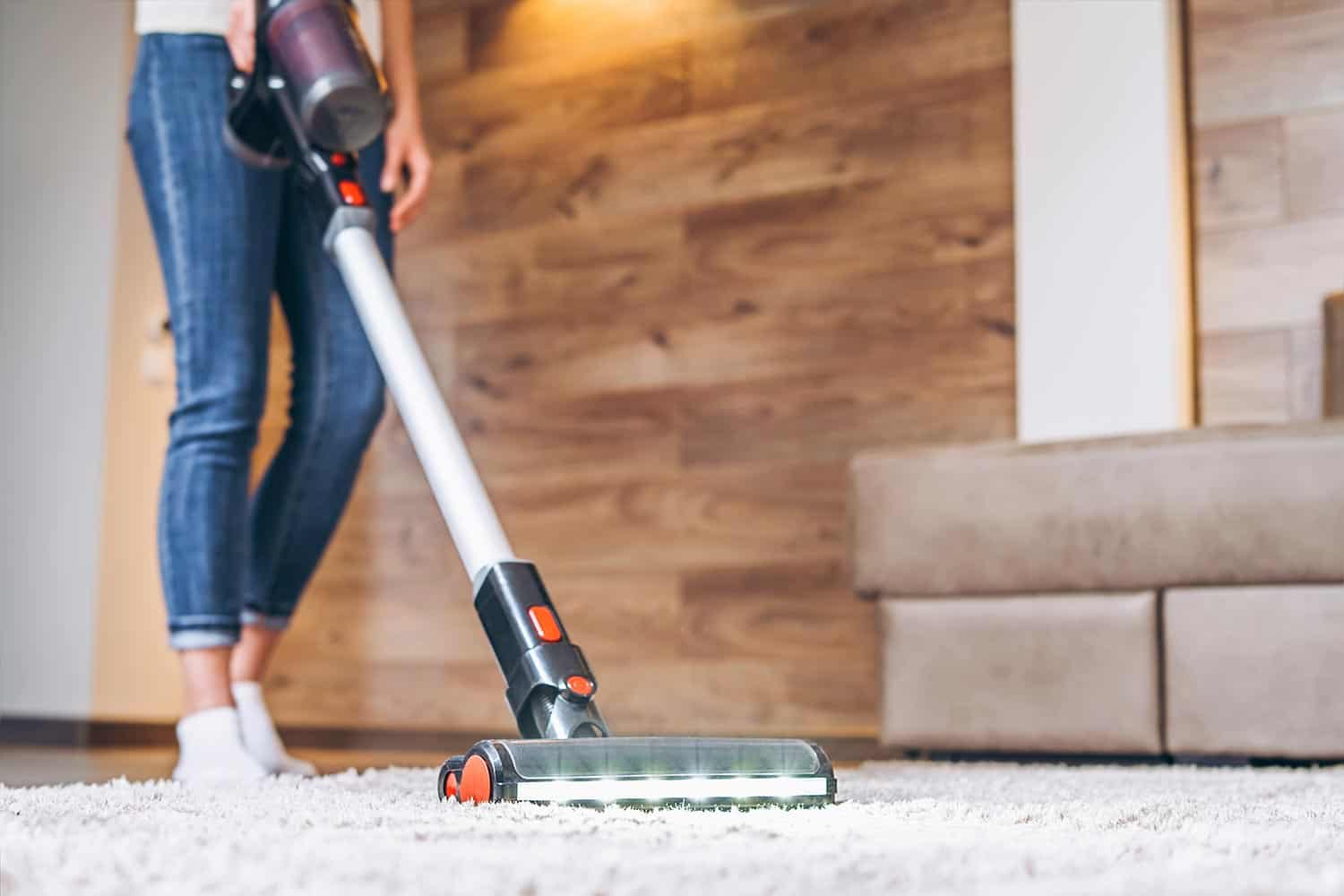 Woman cleaning floor and carpet with cordless vacuum cleaner at home