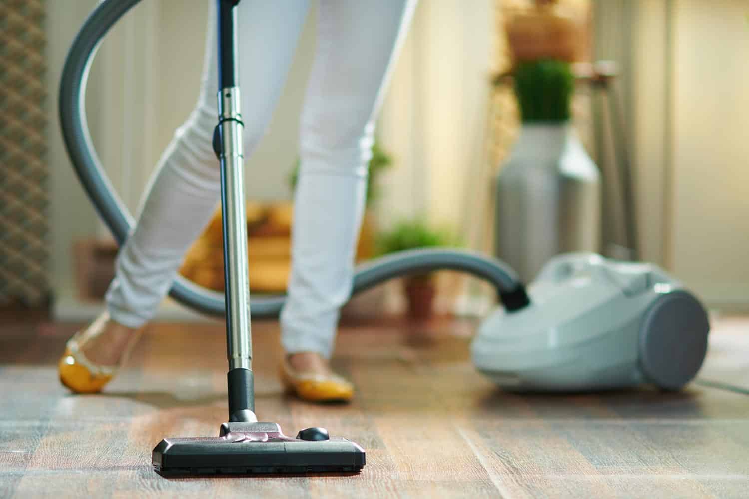 Woman in the living room in sunny day vacuuming floor