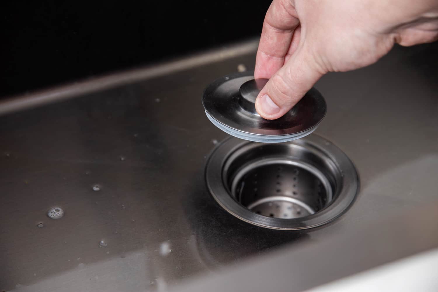 A man's hand holds a plug for a drain hole to fill water. modern kitchen sink