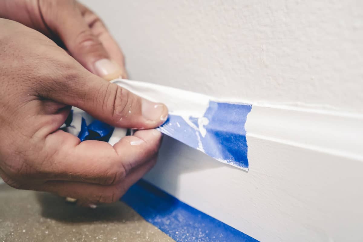A painter pulls of blue painter's tape from the wall to reveal a clean edge