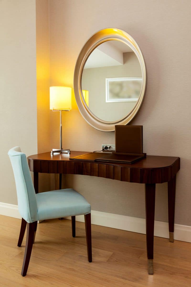 Dark wooden console table with a round mirror on the wall and sky blue chair