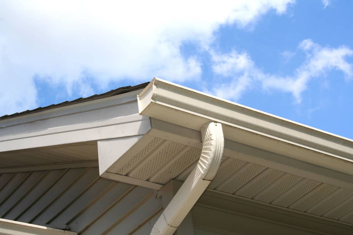 Gutter and downspout of a house with a blue sky and white clouds