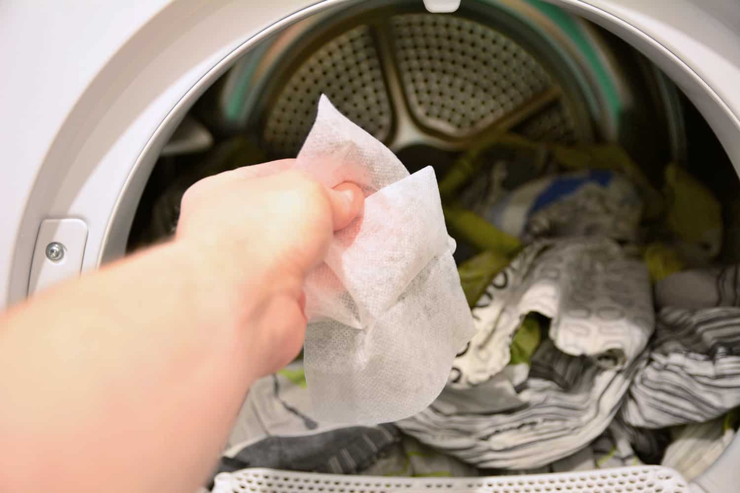 Hand holding and put dryer sheet into a tumble clothes dryer.