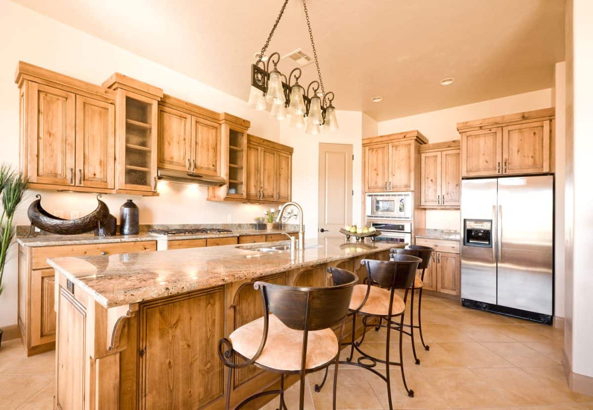 Luxurious modern oak cabinets with beige marble countertops and tan painted walls and mid century inspired chandeliers