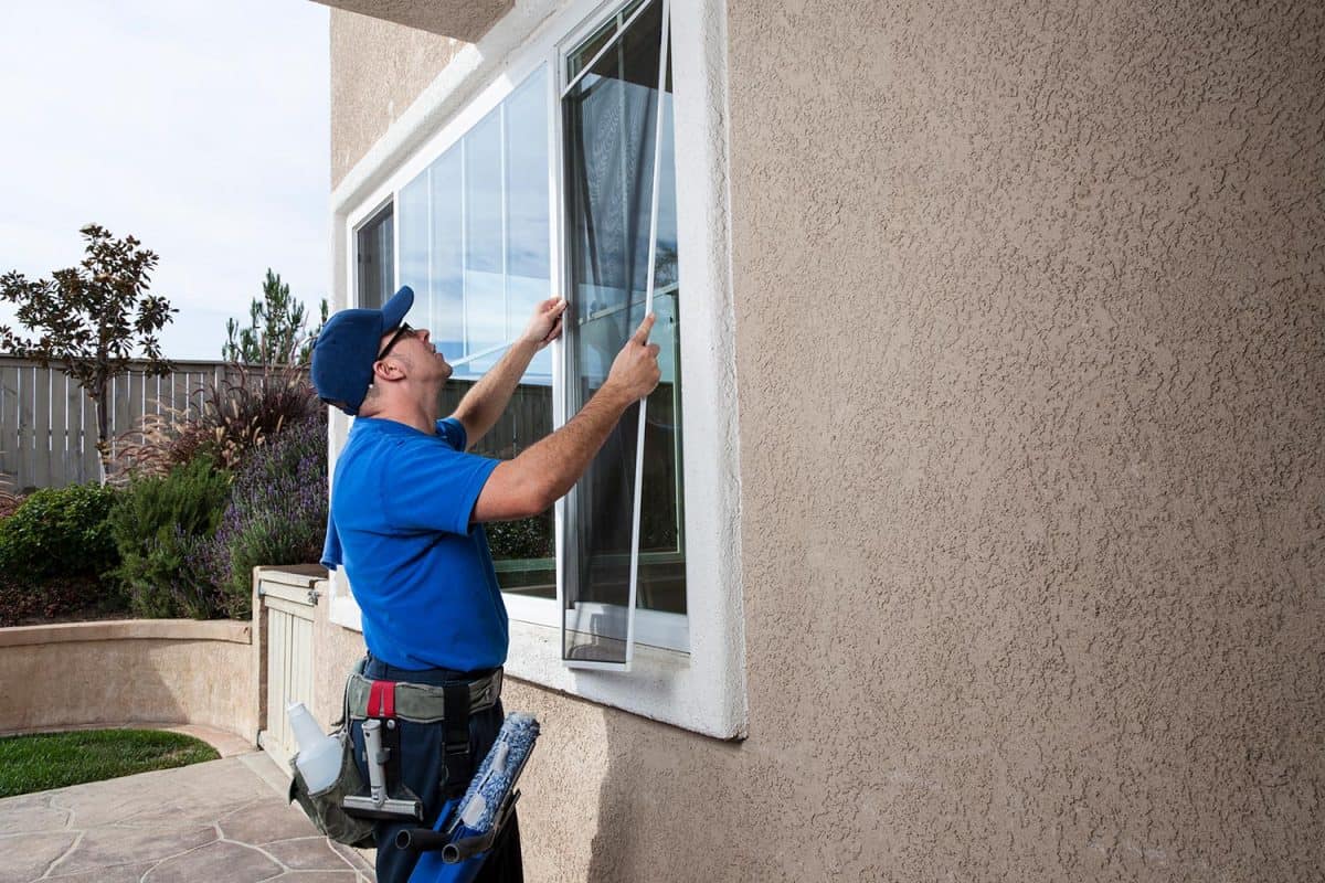 Man cleaning window of a home and installing a screen