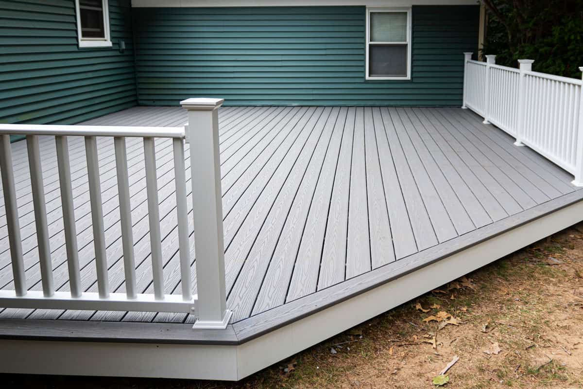 New composite deck on the back of a house with green vinyl siding.with whie railings