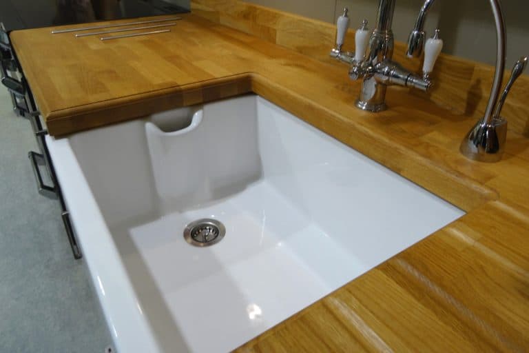 Photo showing a white ceramic Belfast butler sink with chrome mixed taps. The sink is part of a fitted kitchen, surrounded by a real wooden kitchen worktop. - Sink Drain Too Long—What To Do
