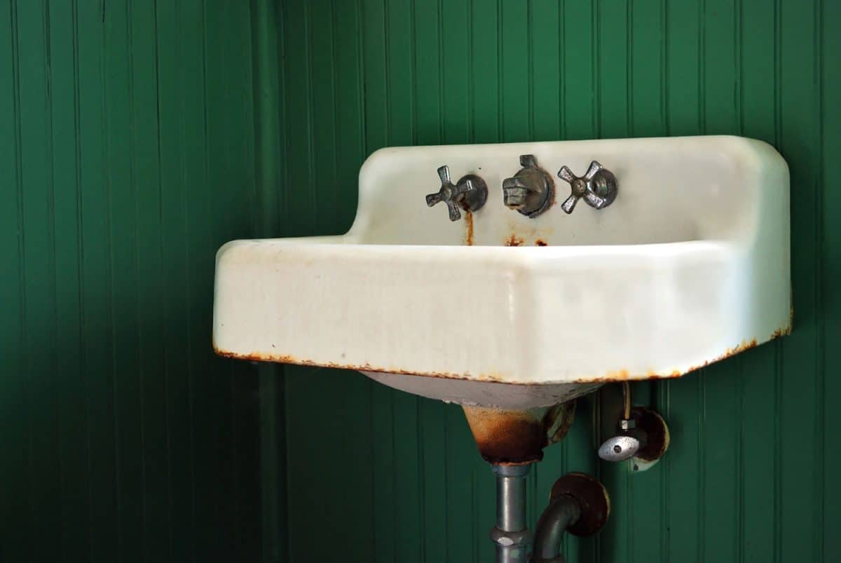 Rusted Old Sink and Fixtures on Green Panel Wall
