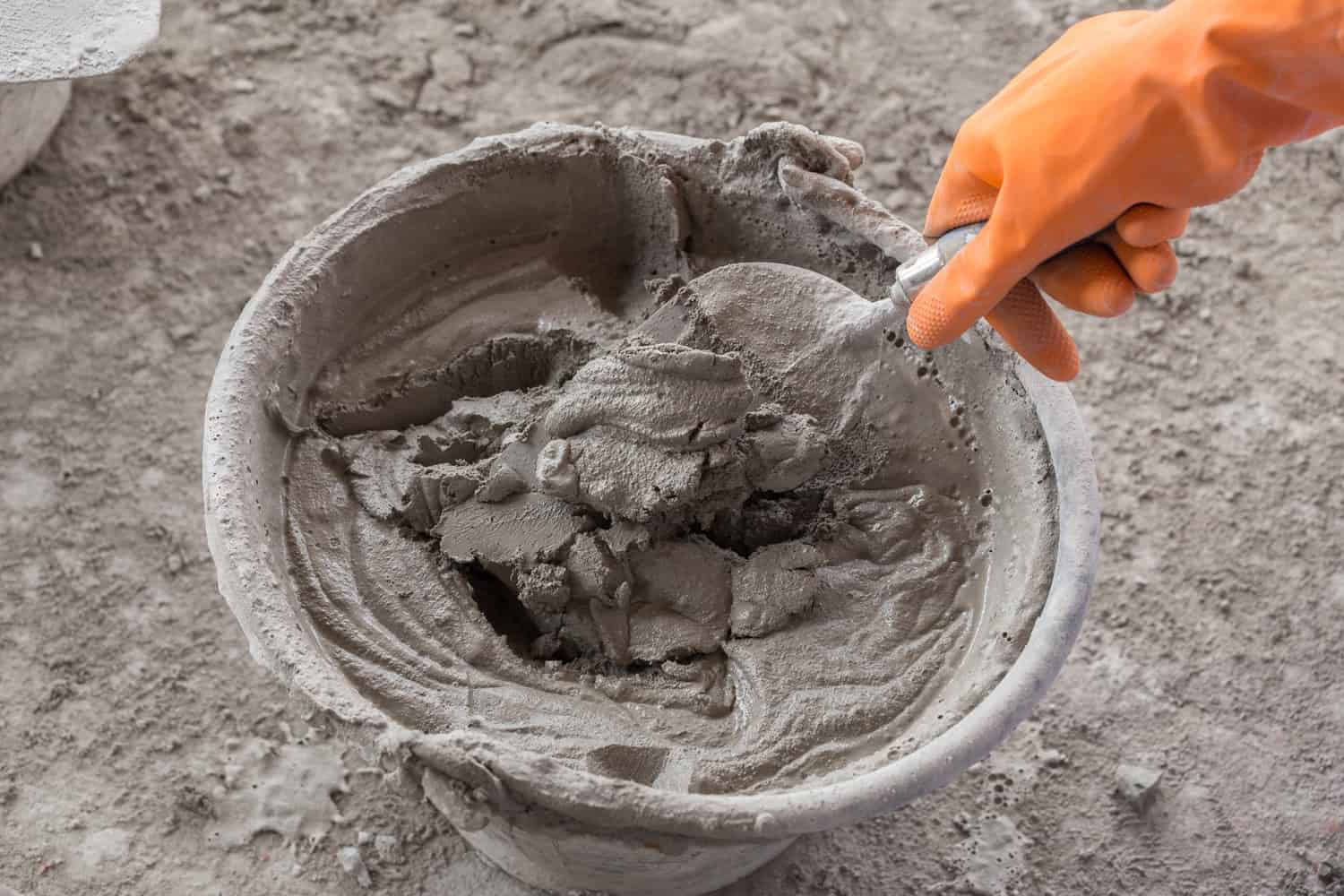 hand with old trowel and bucket with mortar at consturction site