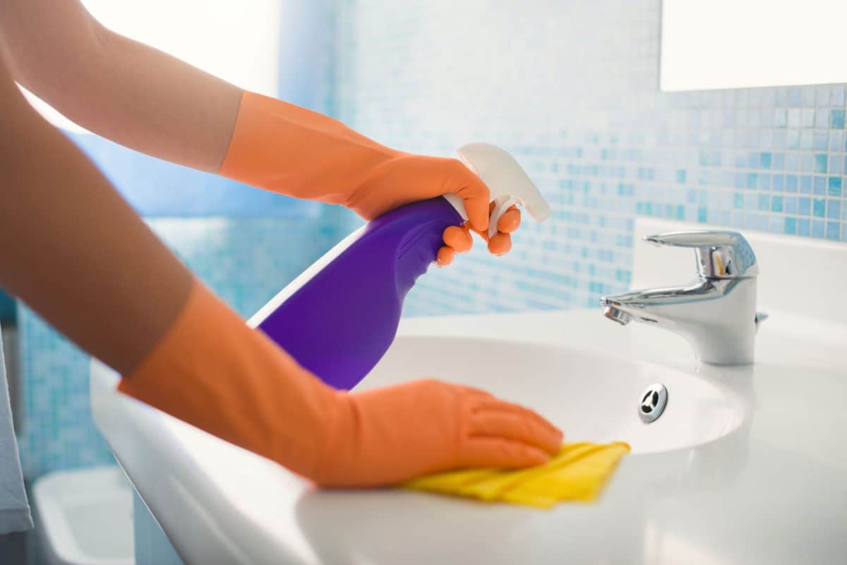woman doing chores in bathroom at home, cleaning sink and faucet with spray detergent.