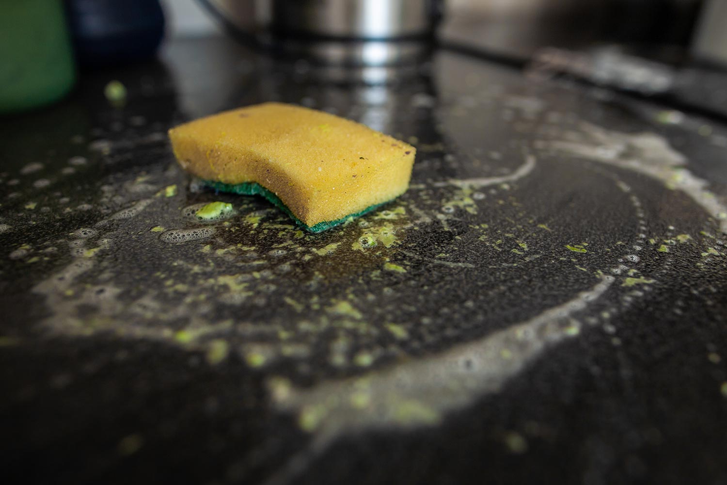 Dirty yellow kitchen sponge on dirty dark countertop with detergent
