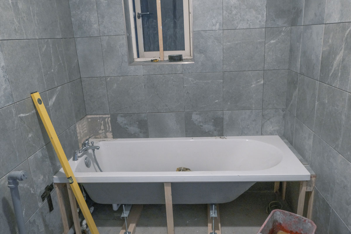 Installing a fitted bathtub with gray tiles and matching gray grout