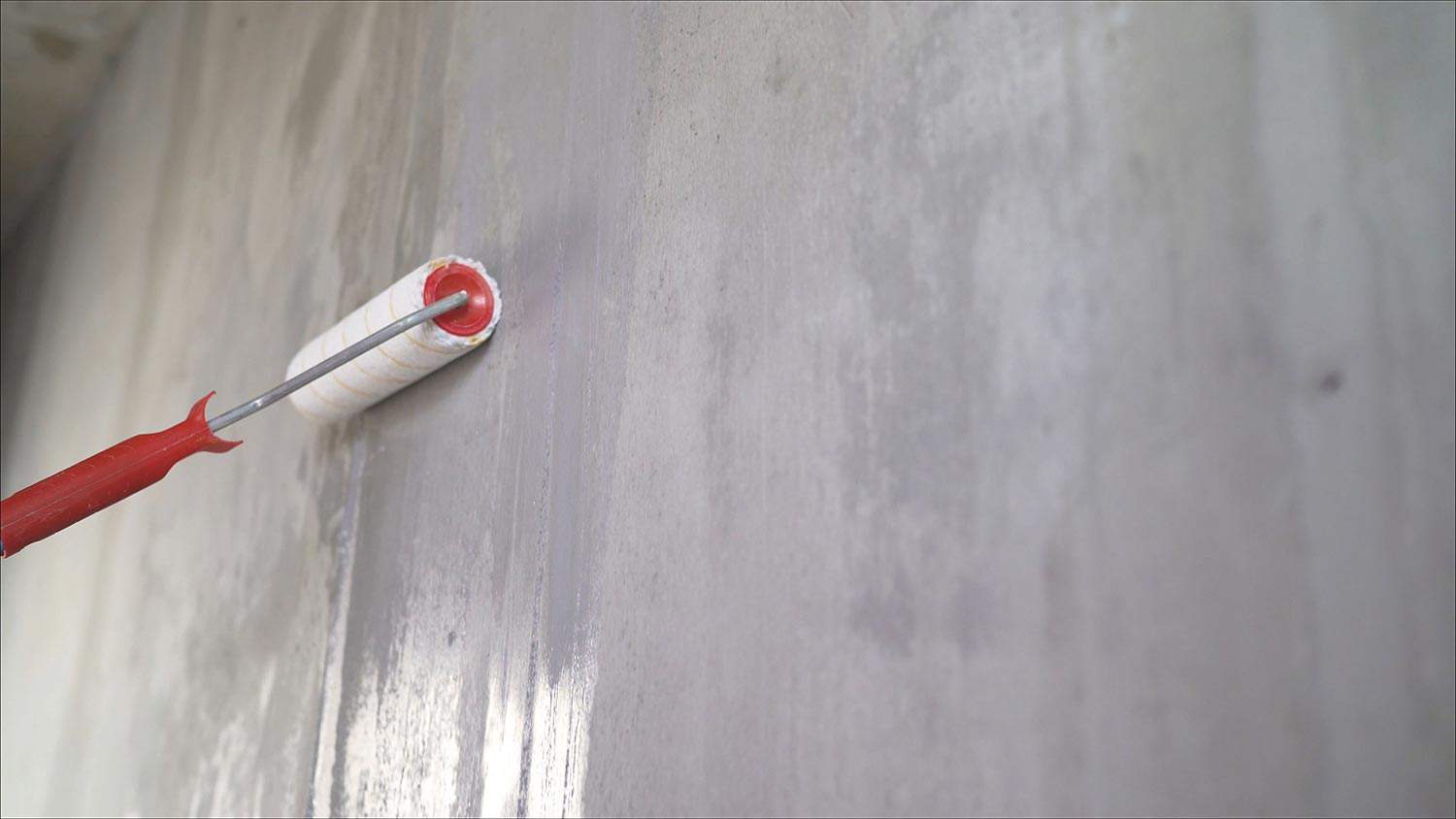 Painting out a bare wall with a paint roller with gray paint