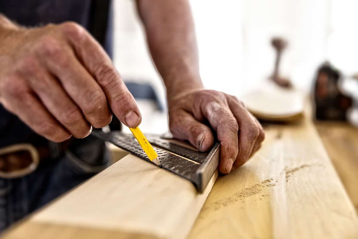 Carpenter using carpenter's square and pencil to mark molding to be cut