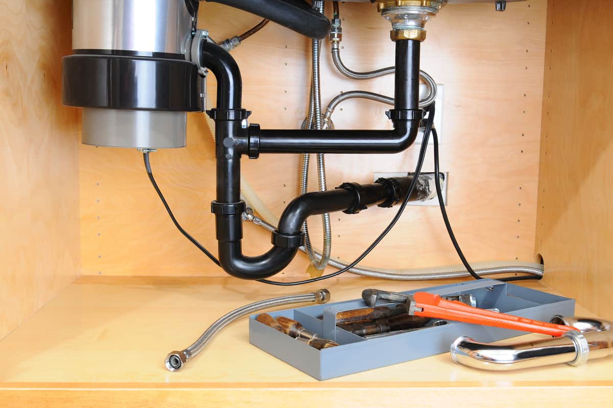 Detail of the plumbing system under a modern kitchen sink, with a plumbers tool tray and equipment